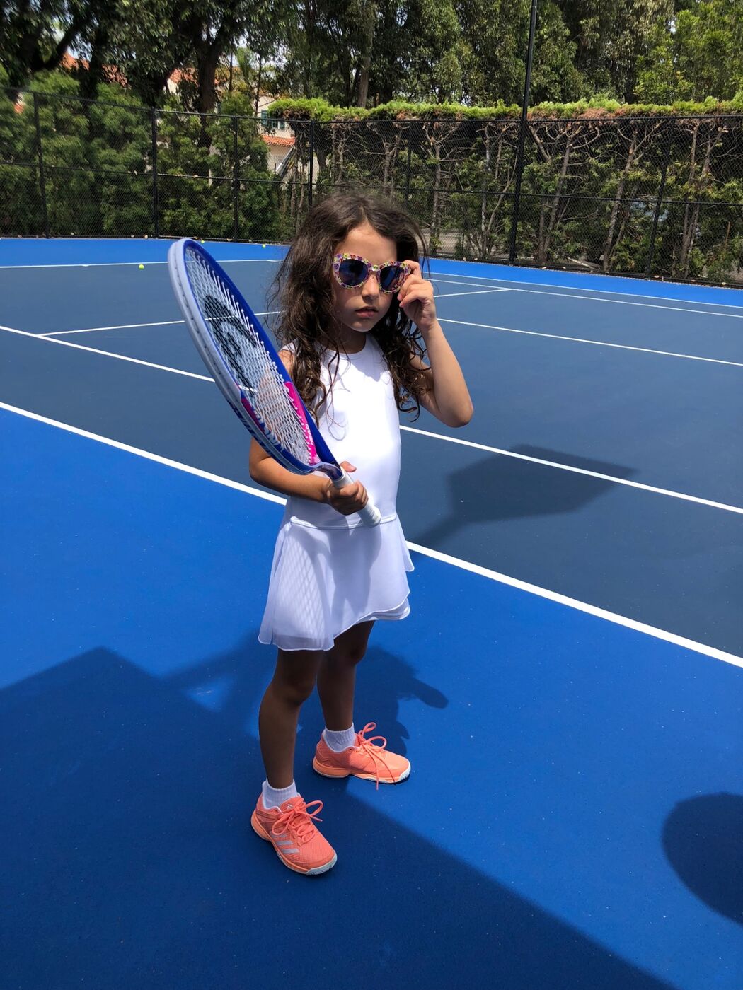 Gabi on a blue court peeking over flower-frame sunglasses