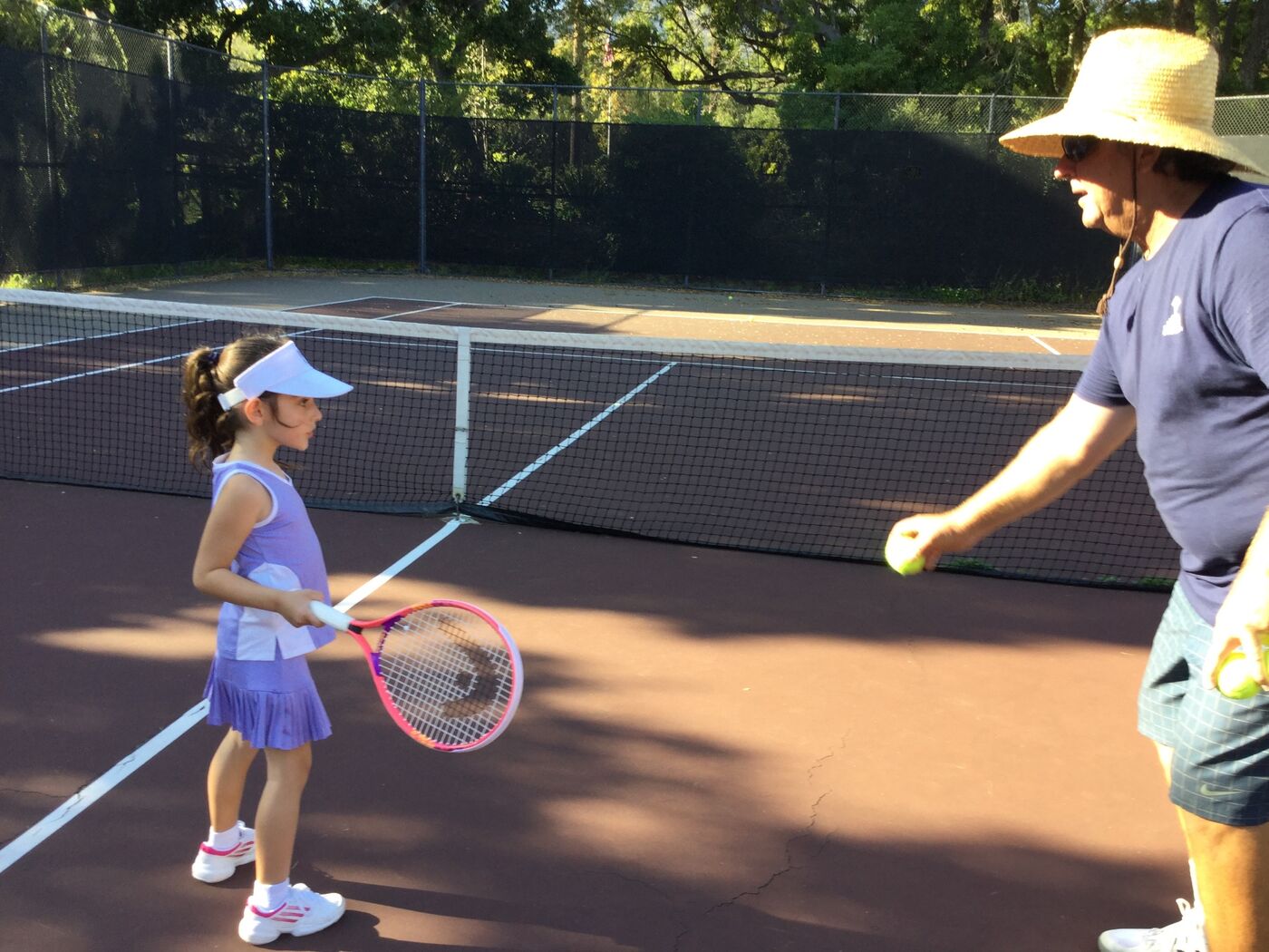 Young Gabi at the net ready to hit with coach feeding balls