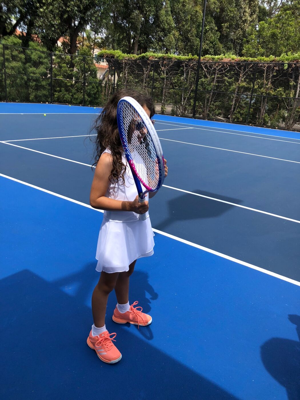 Gabi hiding her face behind her racket on a blue court